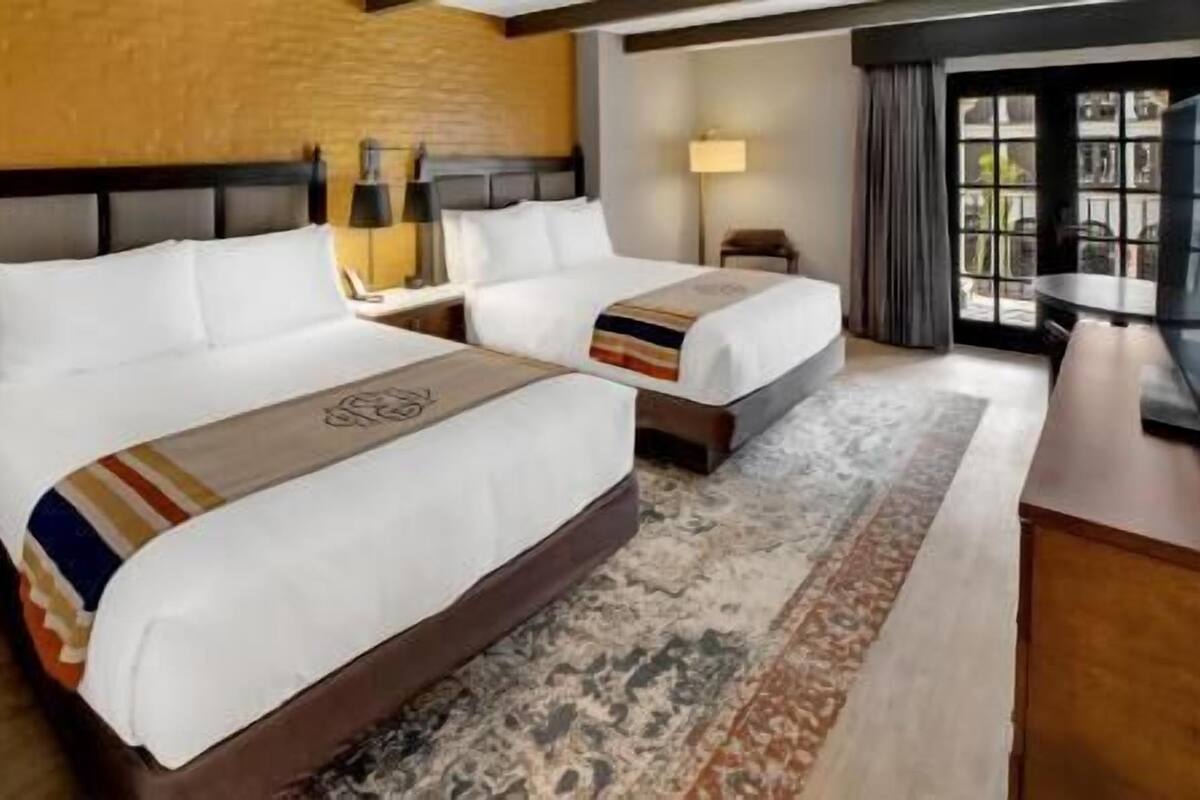 A hotel room with two beds, a large window with curtains, a wooden floor, and a rug.