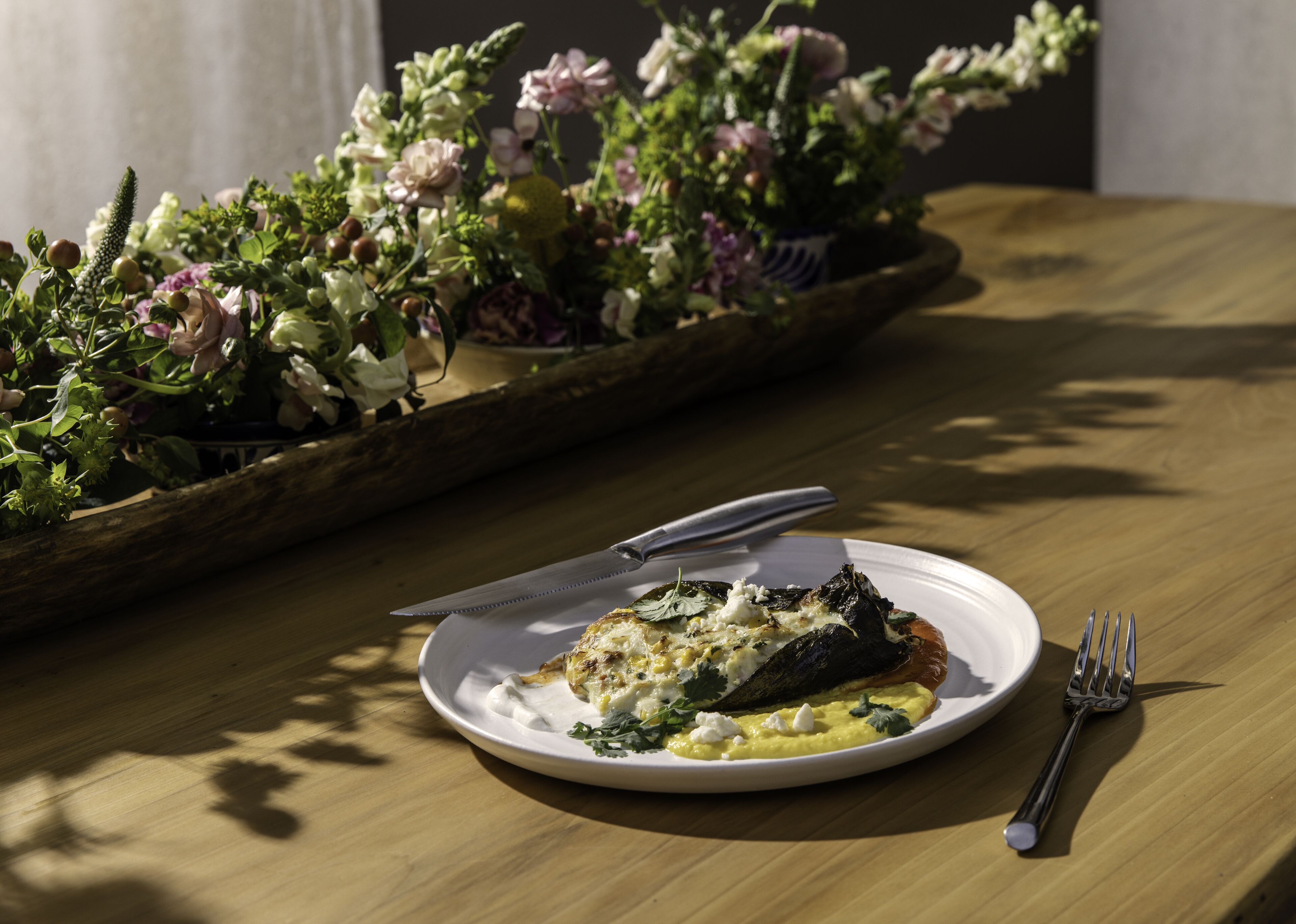 A plate of food on a wooden table with a knife and fork beside it.
