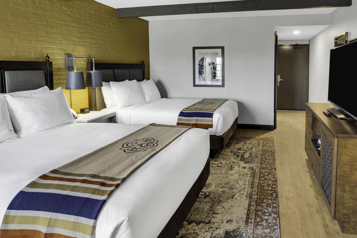 A hotel room with two beds, a television, a desk, and a patterned rug.
