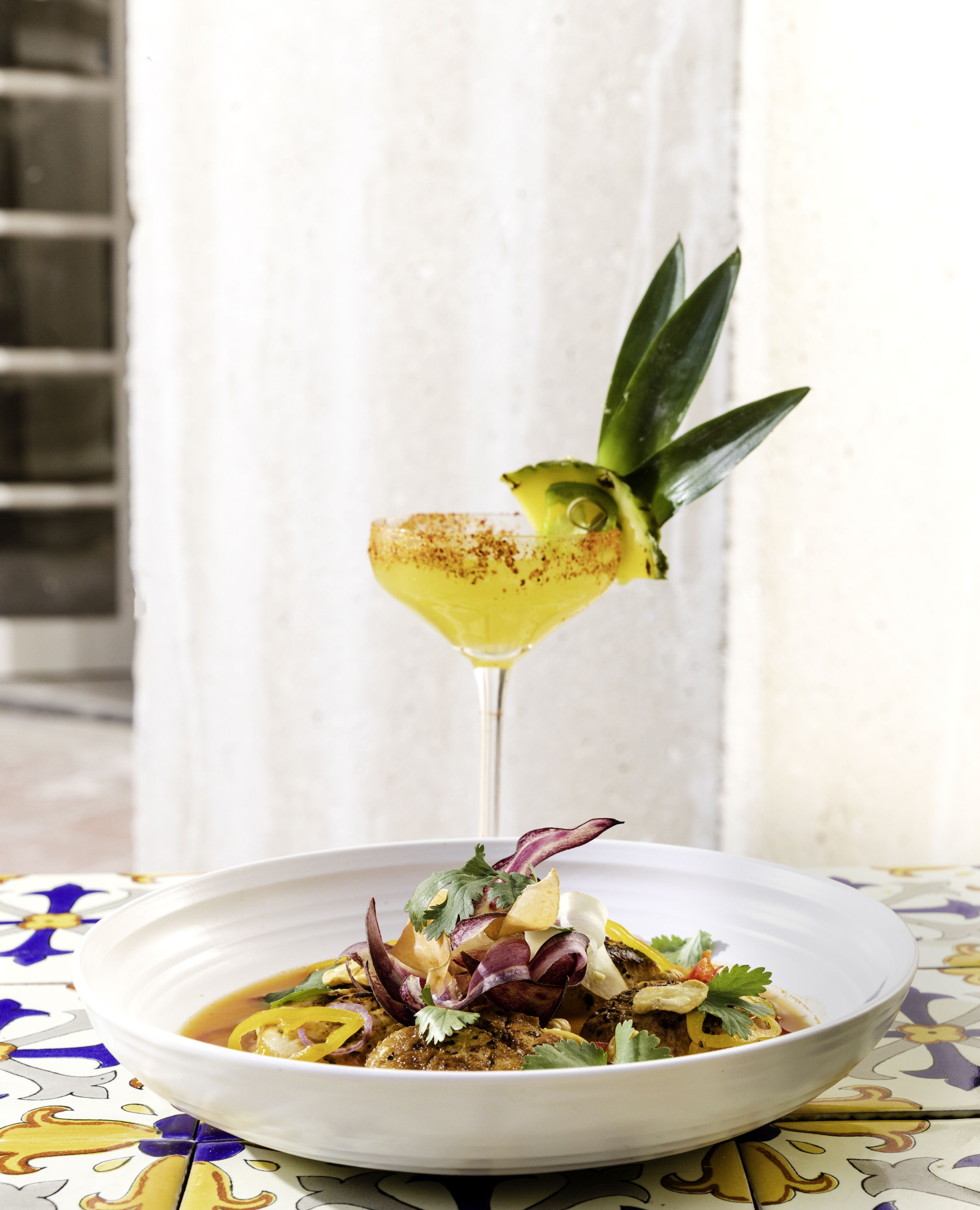 Ein weißer Teller mit Salat und einem Cocktail auf einem Tisch mit gemustertem Tischläufer.