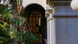 Ein Gebäude mit einem großen Bogenportal, einem Balkon mit Geländer und einem Baum mit grünem Laub im Vordergrund.