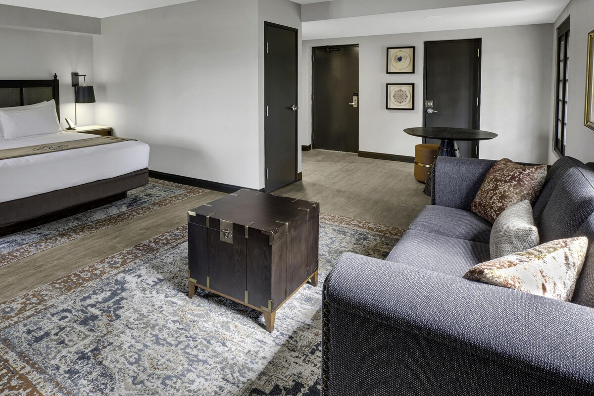Una habitación de hotel con cama, sofá, una mesita y una maleta.