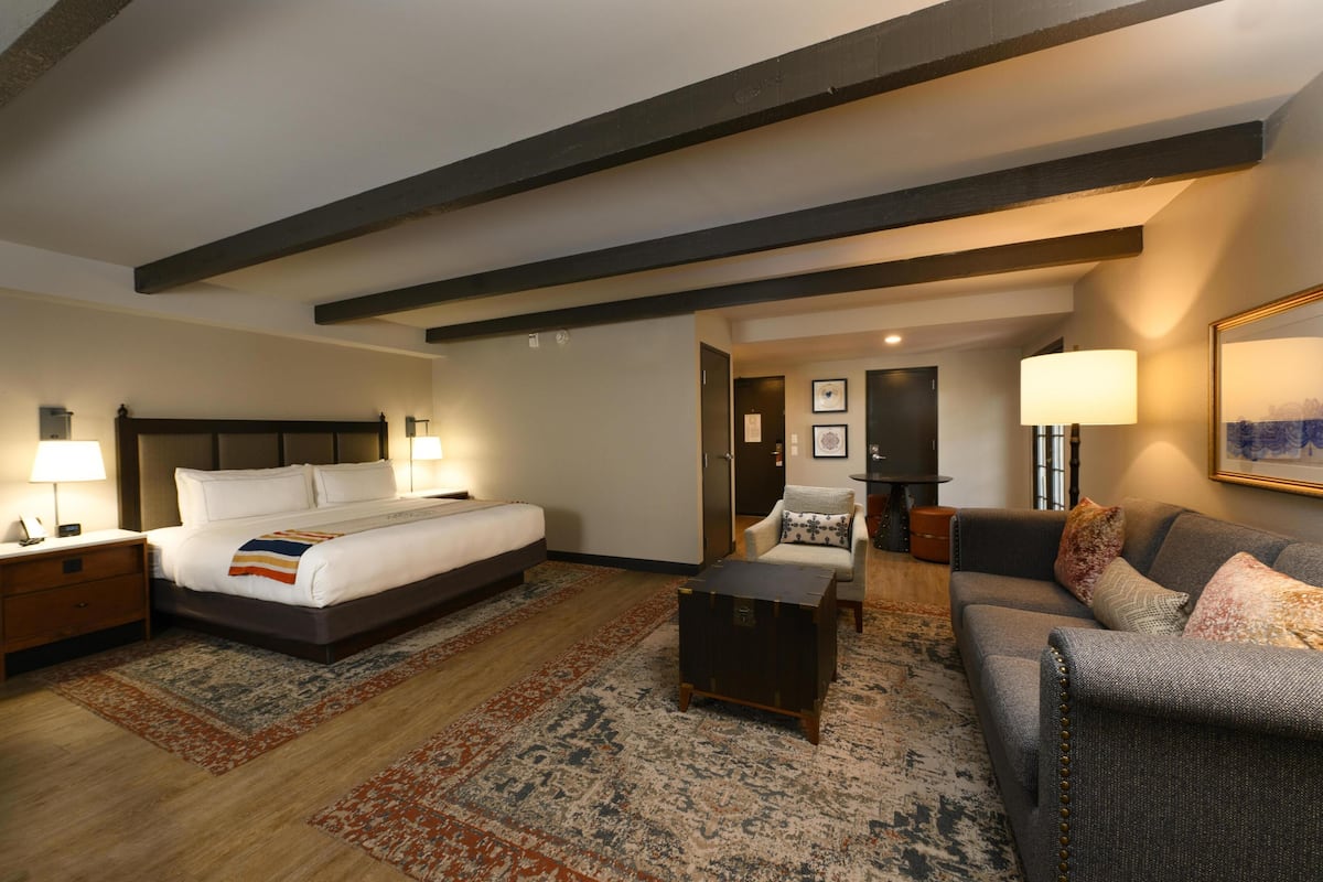 A hotel room with a bed, a sofa, a coffee table, a nightstand, and a lamp.
