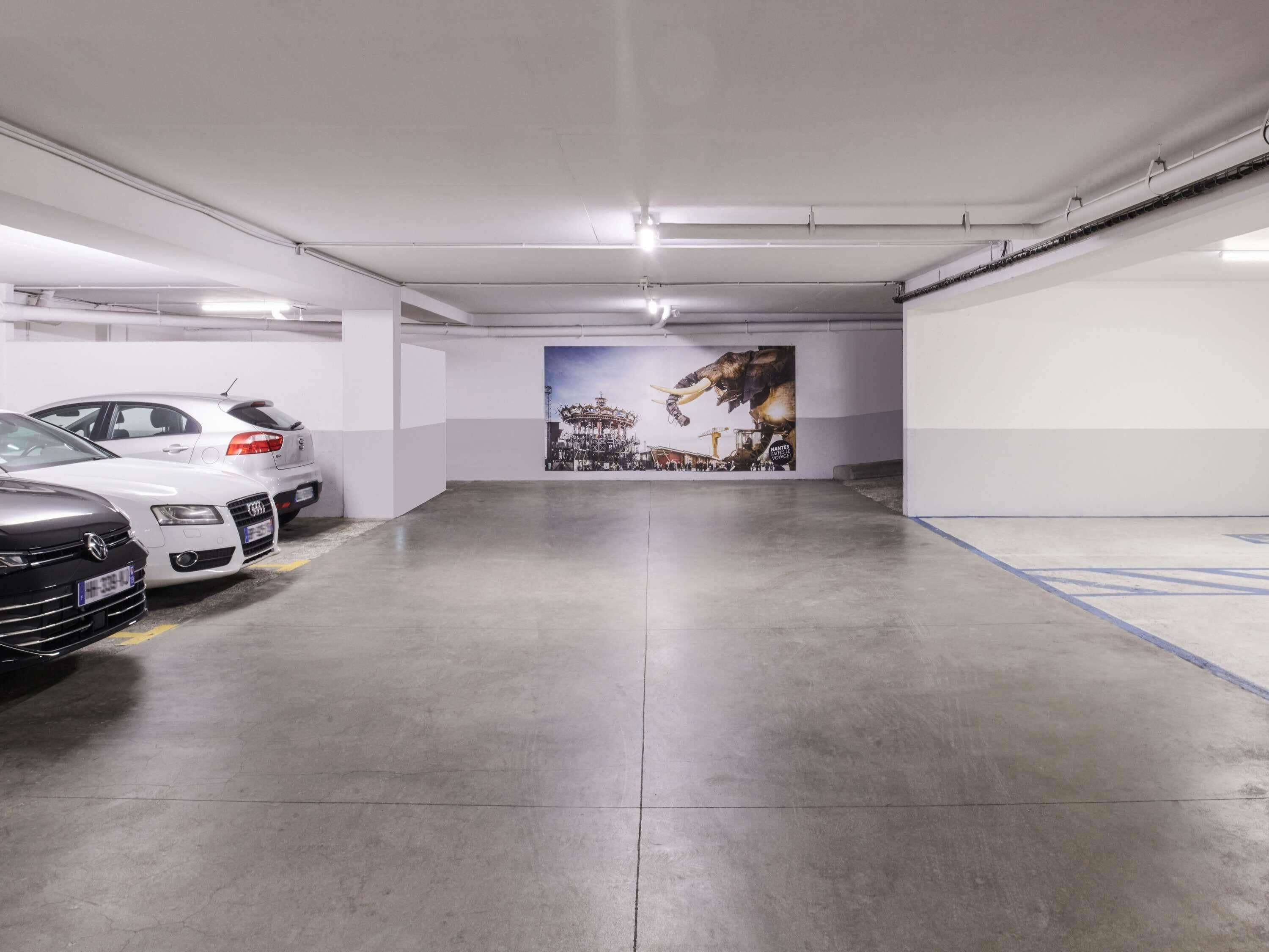 Un estacionamiento con tres coches aparcados, un mural en la pared y suelo de hormigón.