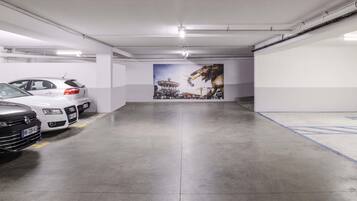 Un estacionamiento con tres coches aparcados, un mural en la pared y suelo de hormigón.