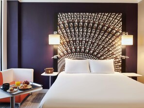 A hotel room with a bed, a table with breakfast, two bedside lamps, and a patterned wall. - Mercure Nantes Centre Grand Hotel (Nantes)