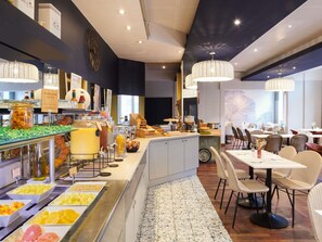 A breakfast buffet with various fruits and beverages, a clock, and a seating area with tables and chairs. - Mercure Nantes Centre Grand Hotel (Nantes)