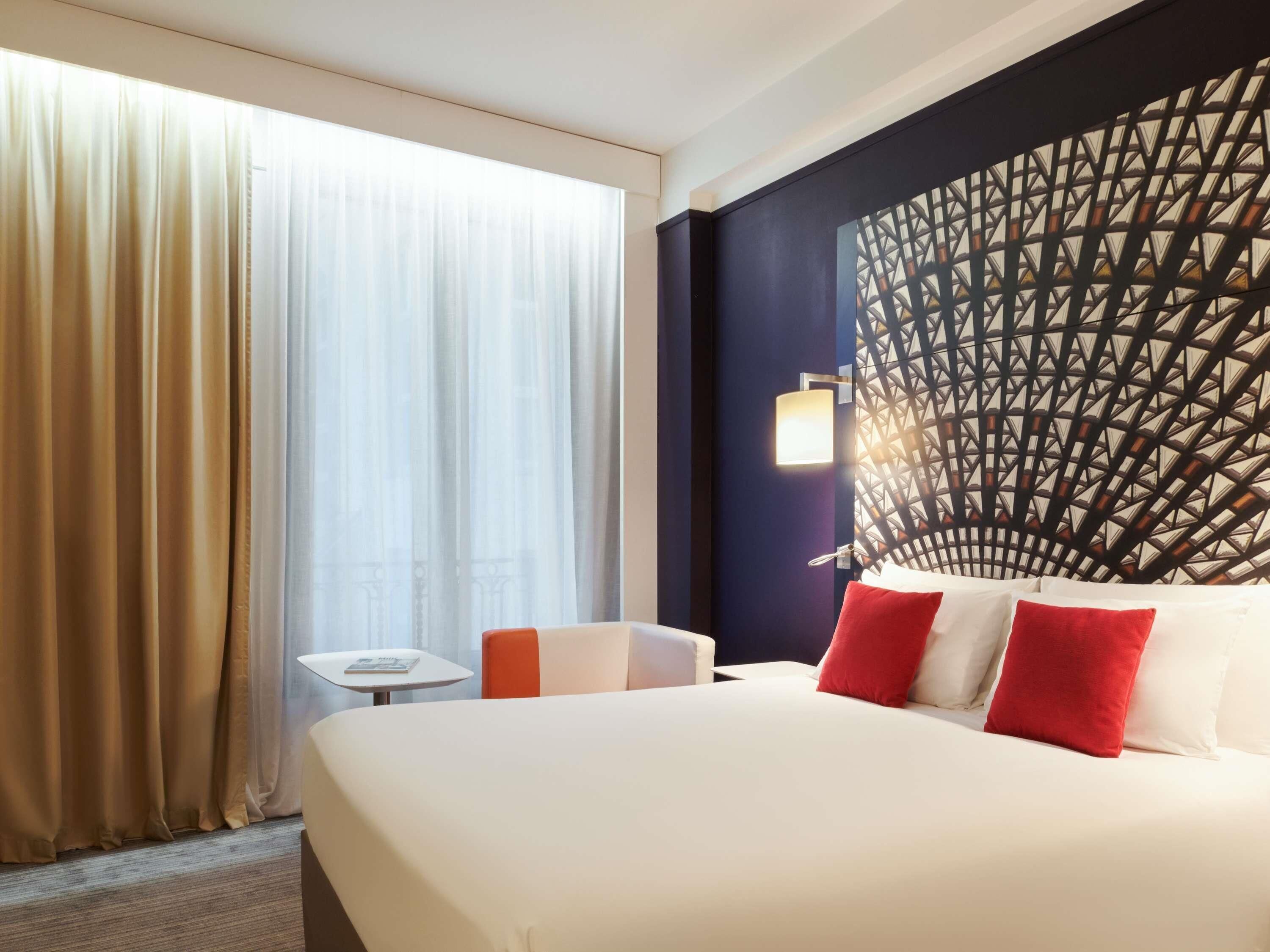 Una habitación de hotel con una cama grande, una mesita pequeña y un adornado en la pared.