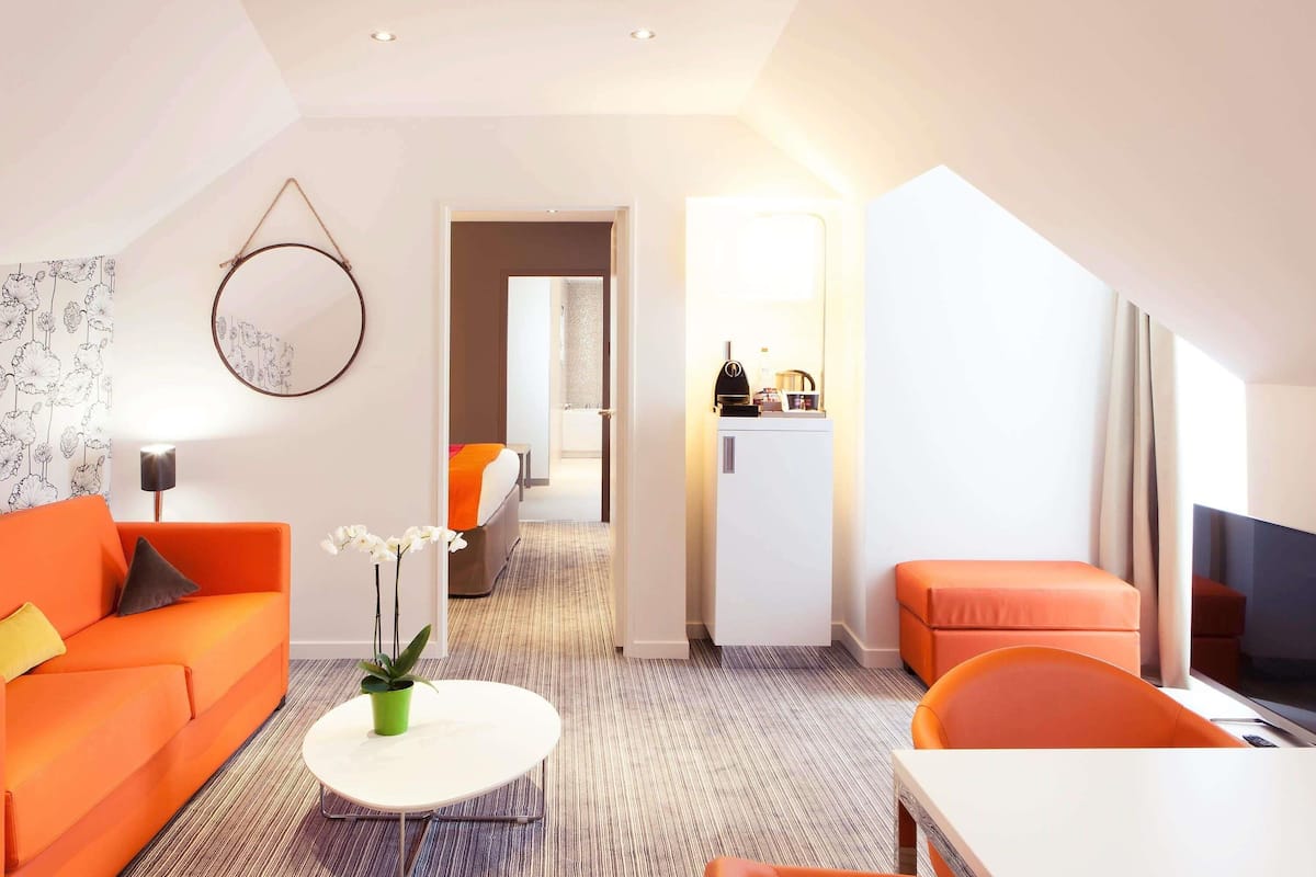 Een moderne hotelkamer met een bank, een eettafel, een klein koffiehoekje en uitzicht op de gang.