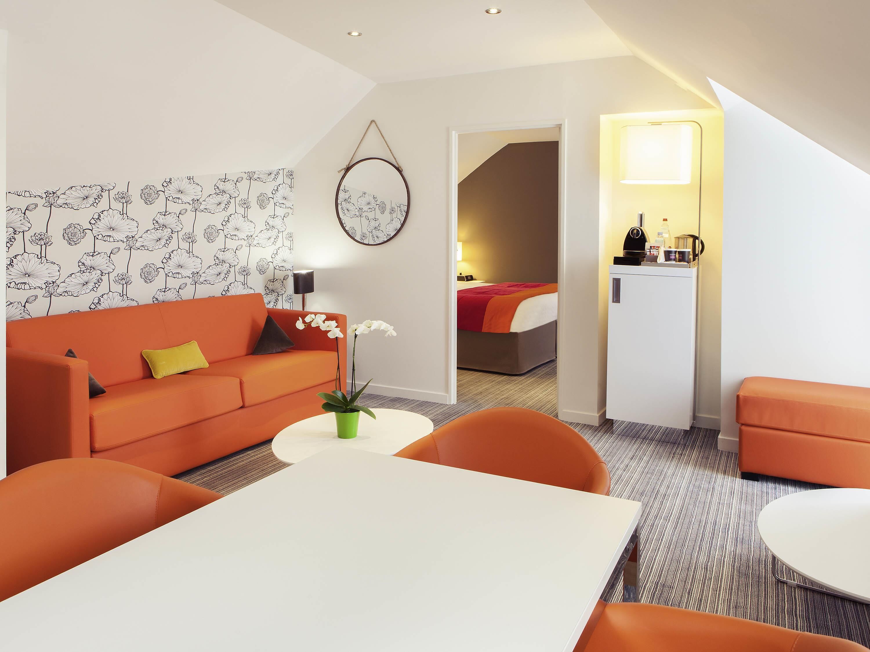 Ein modernes Hotelzimmer mit einer Couch, einem Esstisch, einem Bett und einer Küchenzeile.