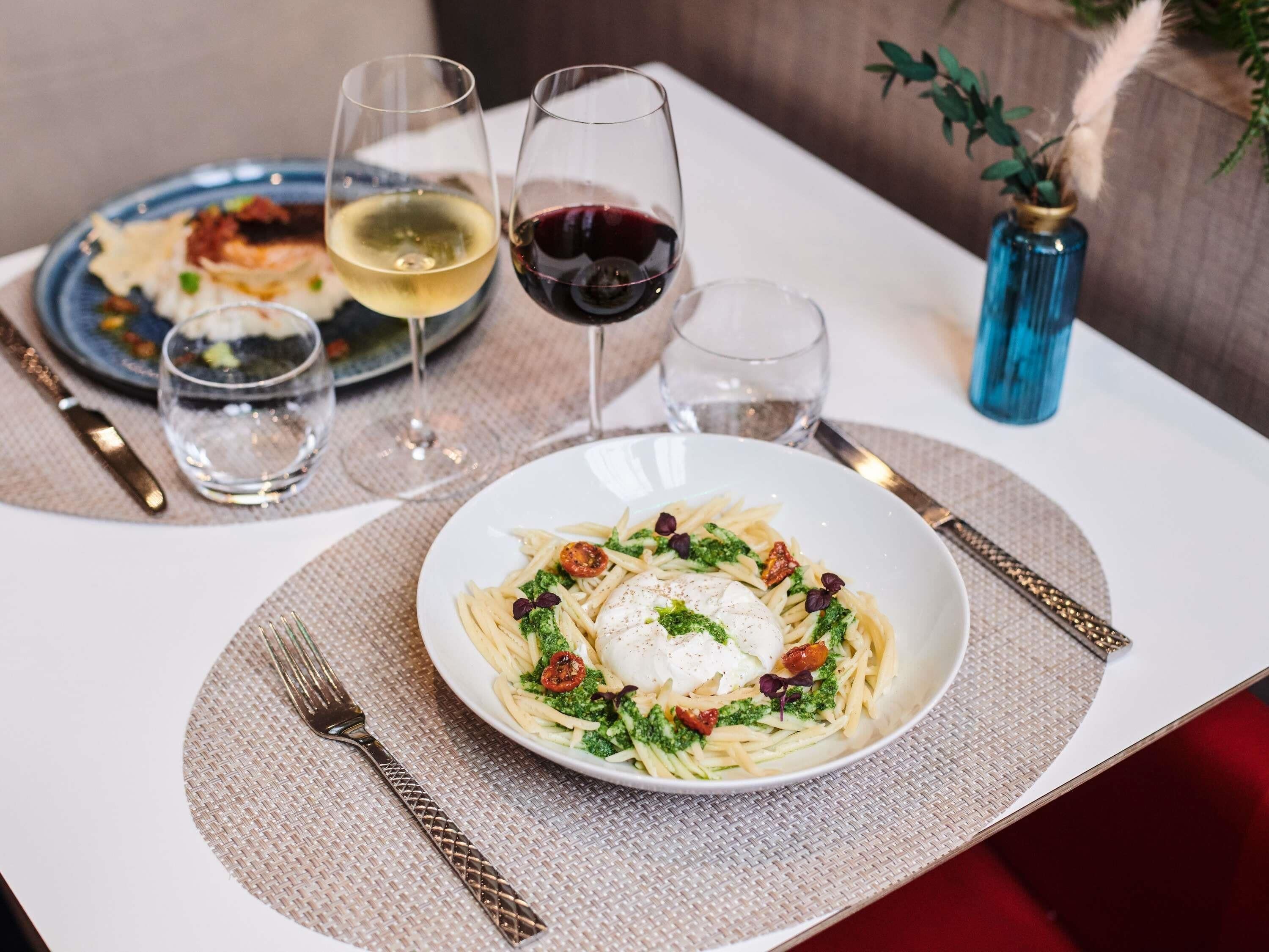 Une table à manger avec des assiettes de pâtes, des verres de vin et des couverts.
