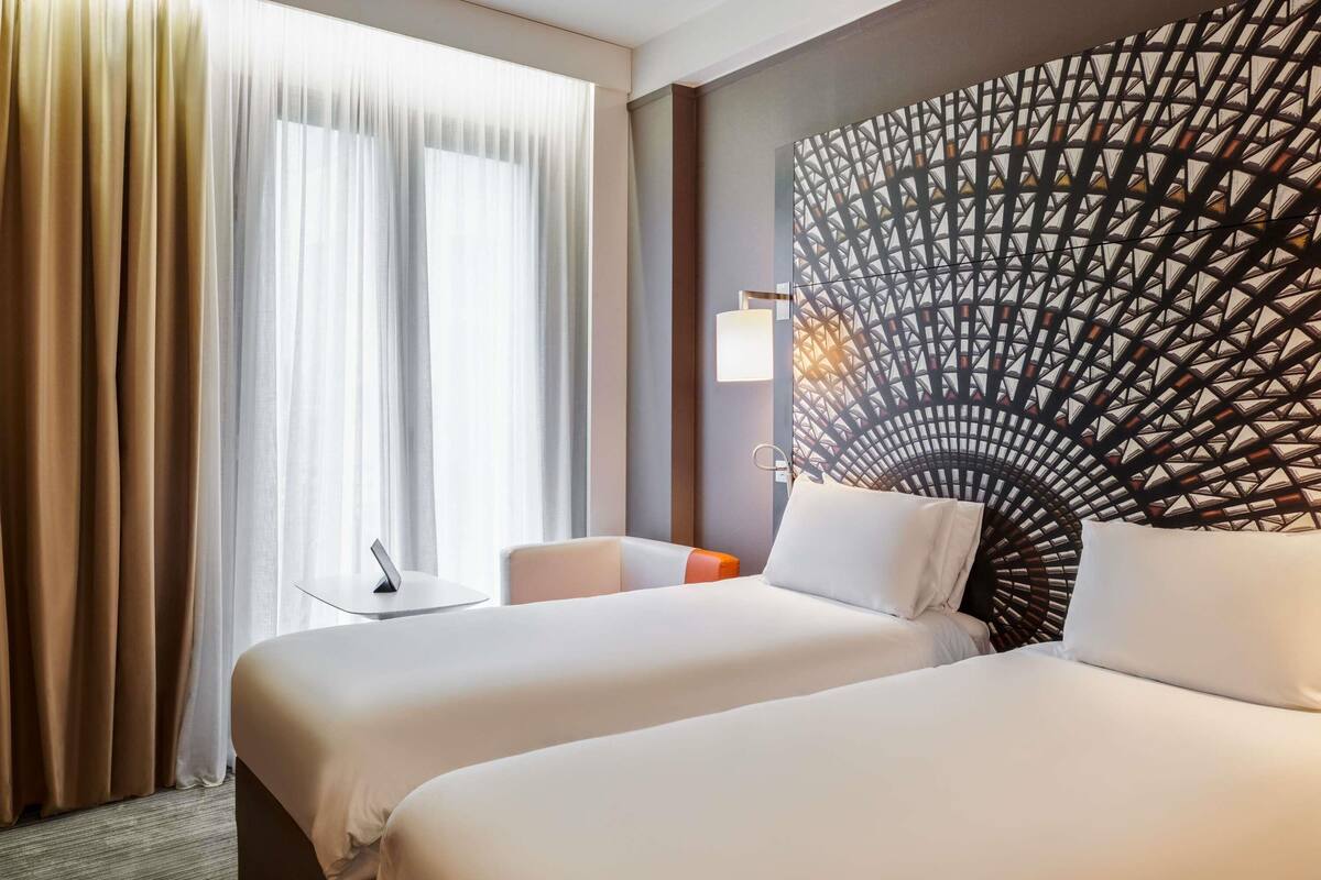 Una habitación de hotel con dos camas, una mesita, una lámpara y un panel decorativo en la pared.