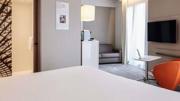 Une chambre d’hôtel avec un lit, un bureau avec un ordinateur portable, une télévision, une chaise et une affiche accrochée au mur.