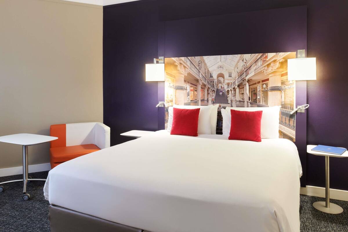 Una habitación de hotel con cama, una silla, una mesita y una lámpara.
