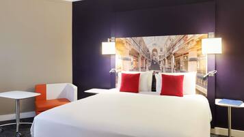 A hotel room with a bed, a chair, a small table, and a lamp.