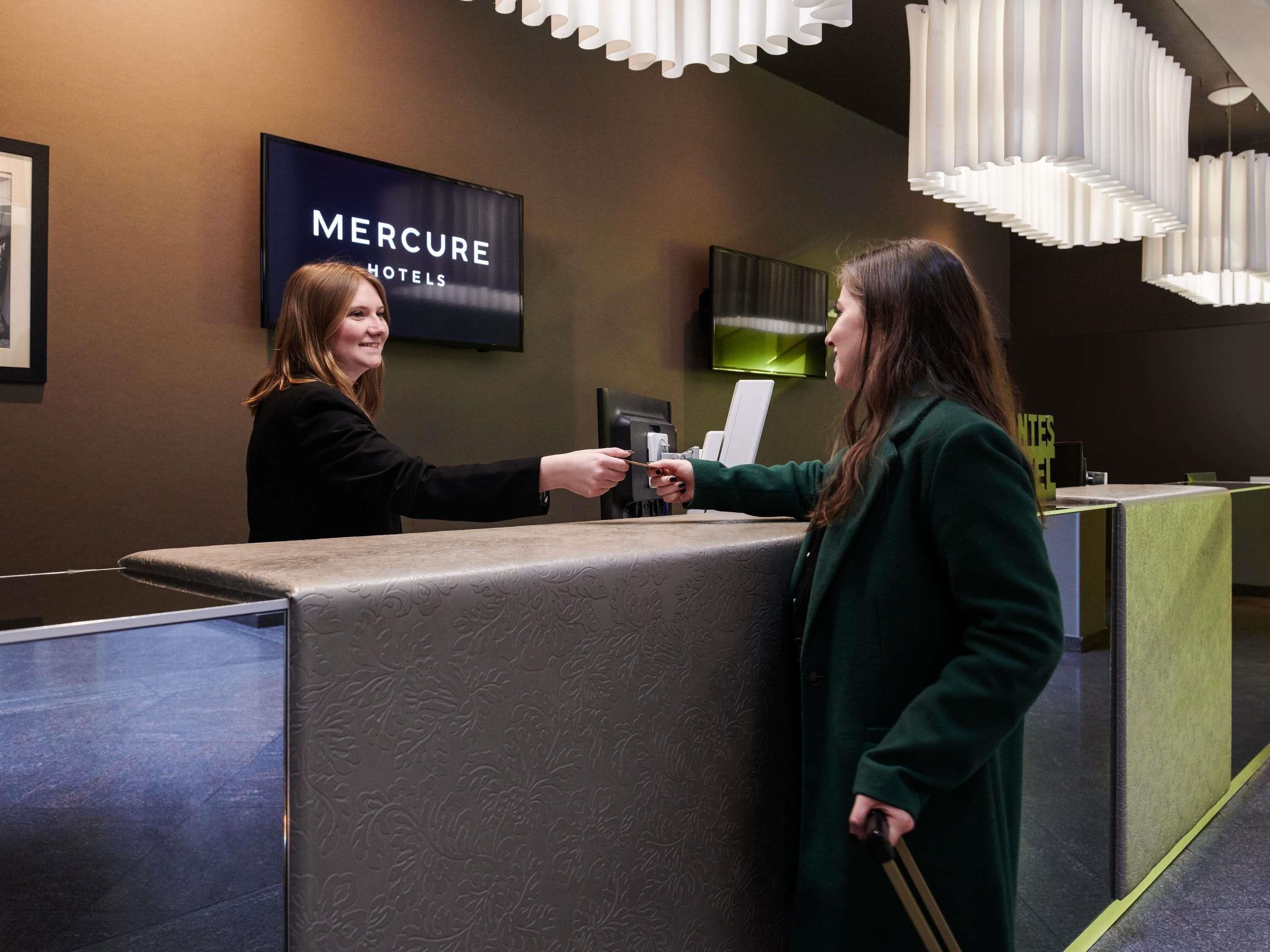 A reception area with a 'Mercure Hotels' sign, a reception desk, and a modern light fixture.