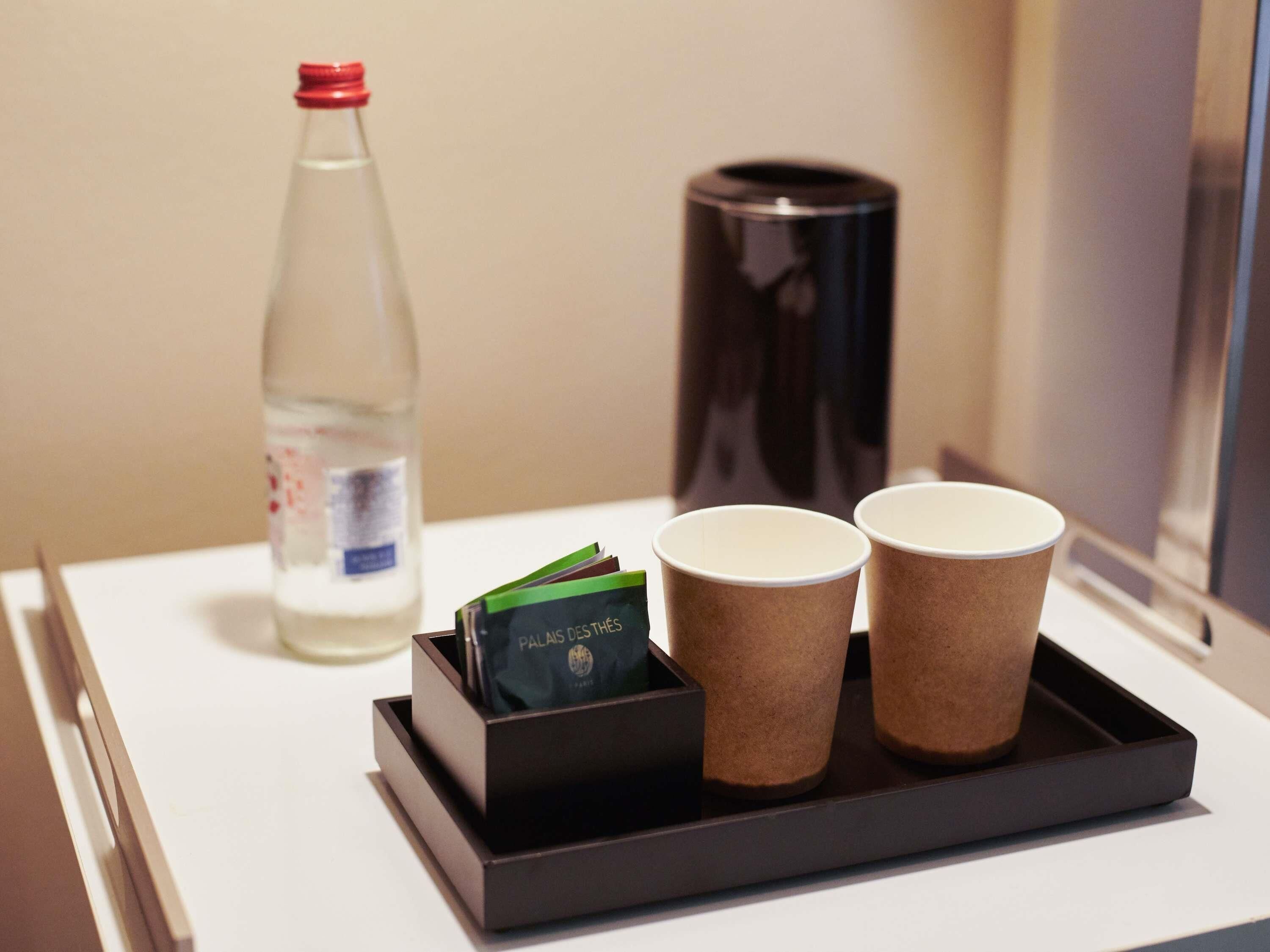 Un safata amb dues tasses de paper, una ampolla d'aigua i un recipient negre amb una targeta.