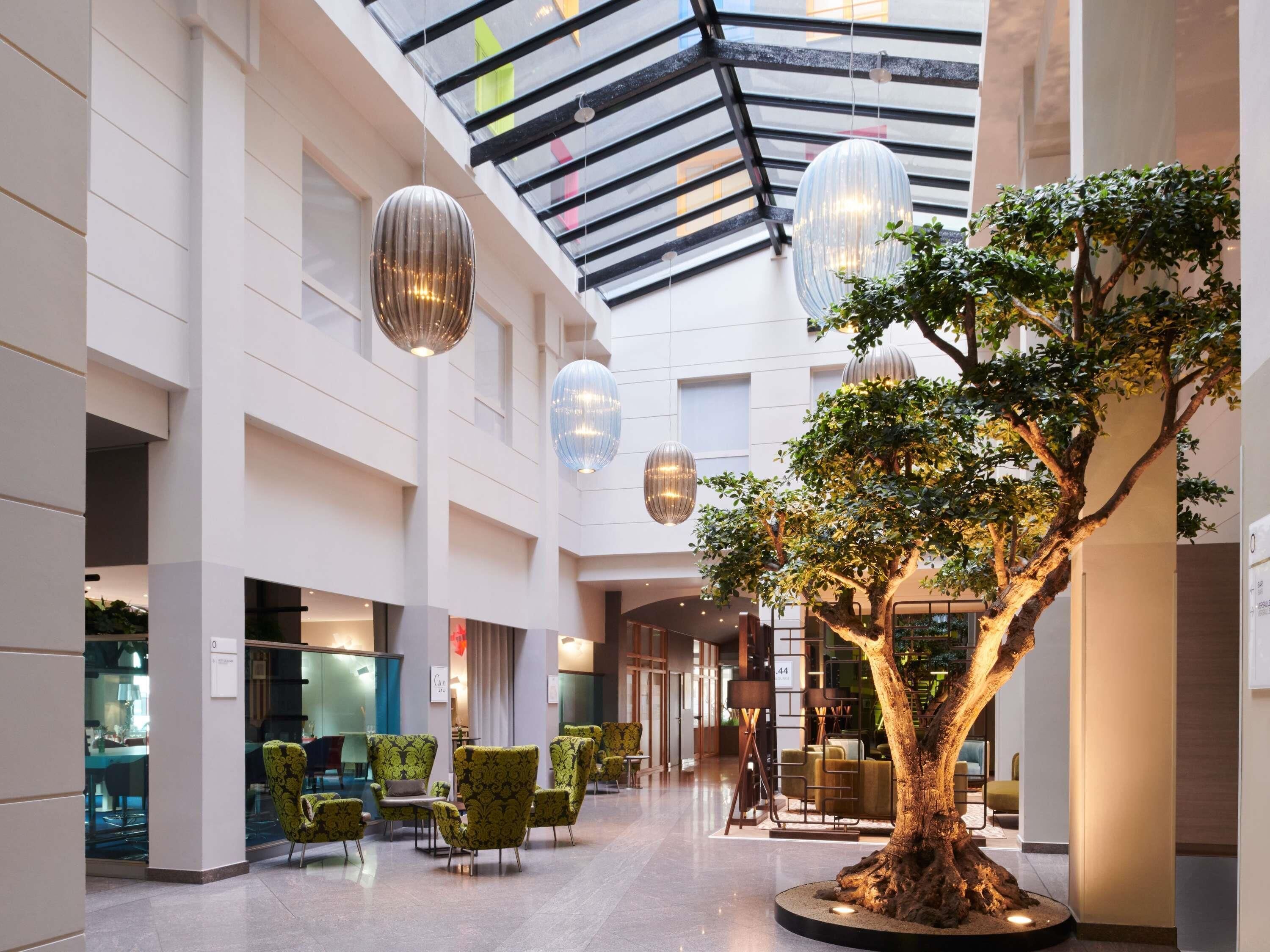 A spacious indoor area with a central tree, modern furniture, and hanging spherical light fixtures.