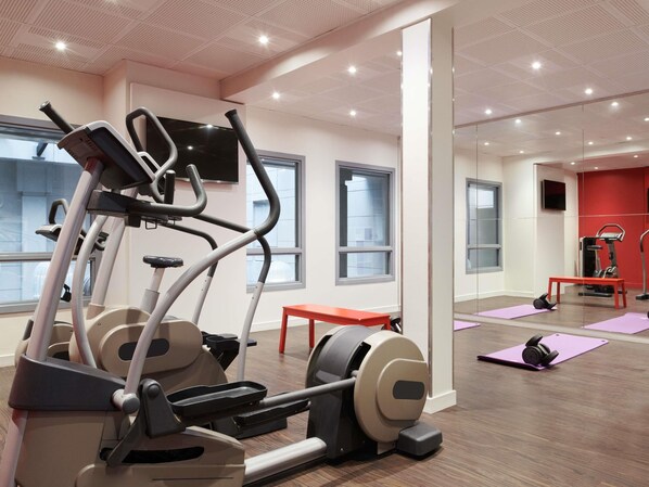 Une salle de sport équipée de matériel d’exercice, d’un banc et d’un miroir.
