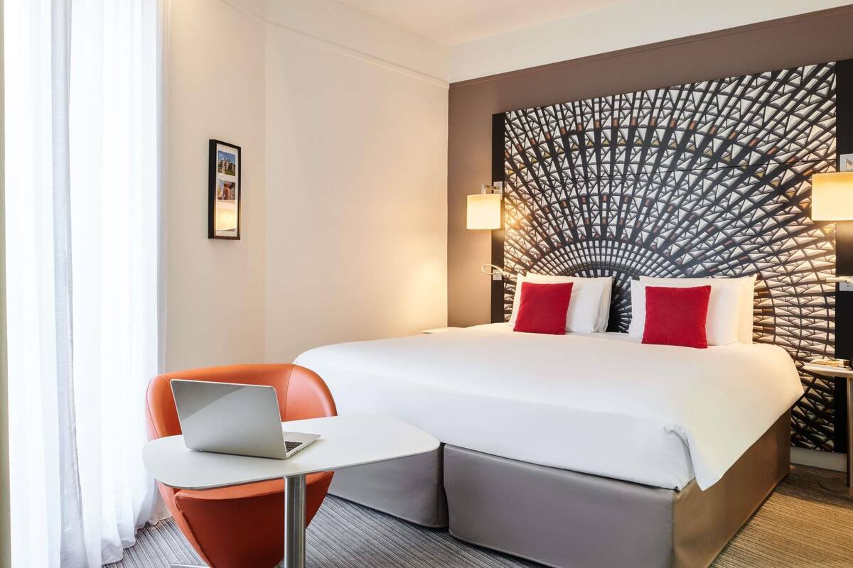 Habitación de hotel con cama, escritorio con ordenador portátil, silla y decoración en la pared.