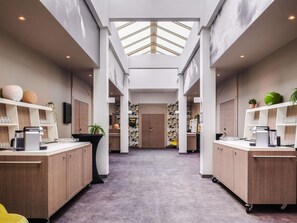 Un hall d’hôtel moderne avec un couloir central, des meubles en bois et un plafond haut doté de lucarnes.