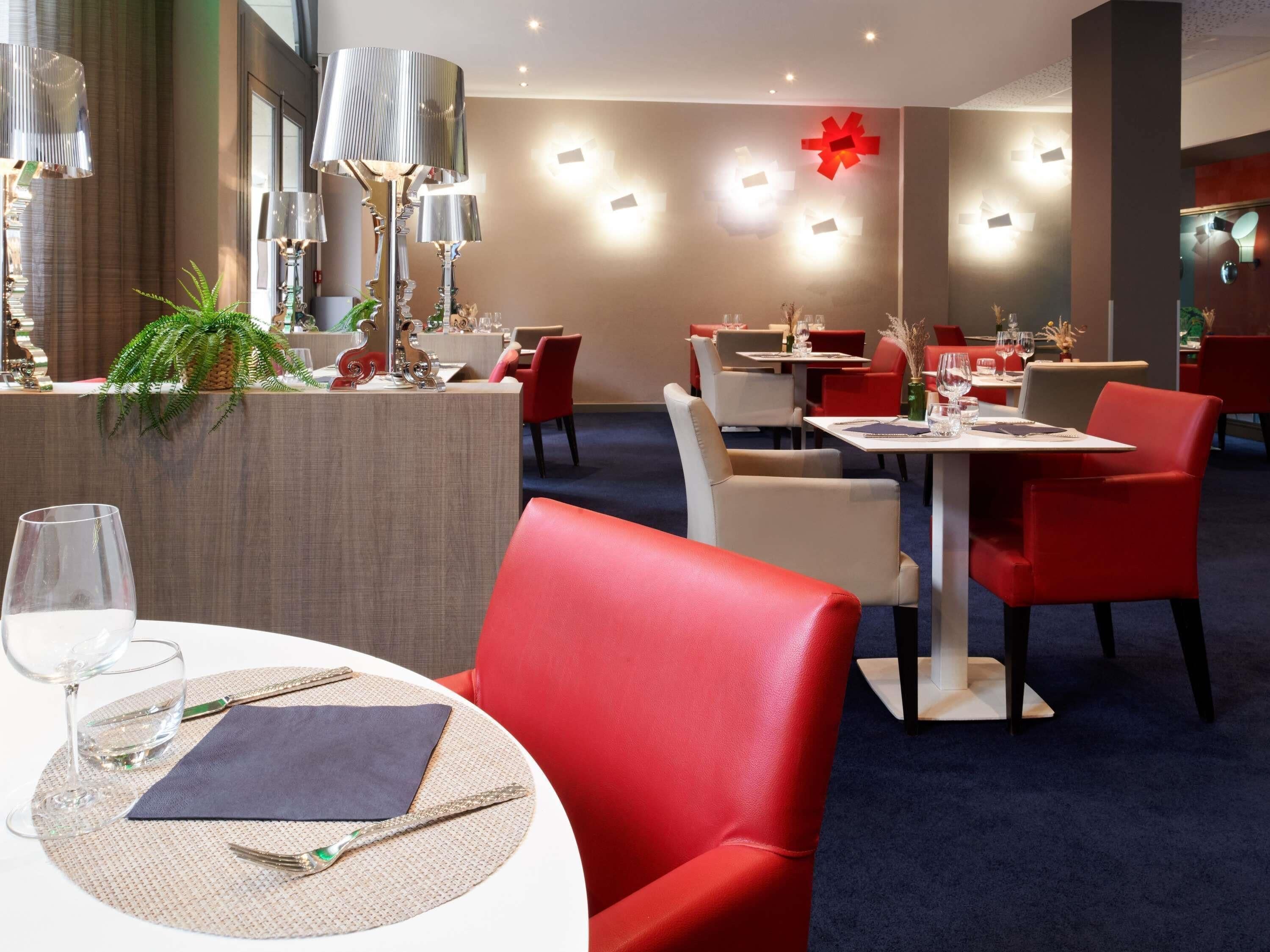 L’intérieur d’un restaurant moderne, avec des tables rondes, des chaises rouges et blanches, et des appliques murales décoratives.