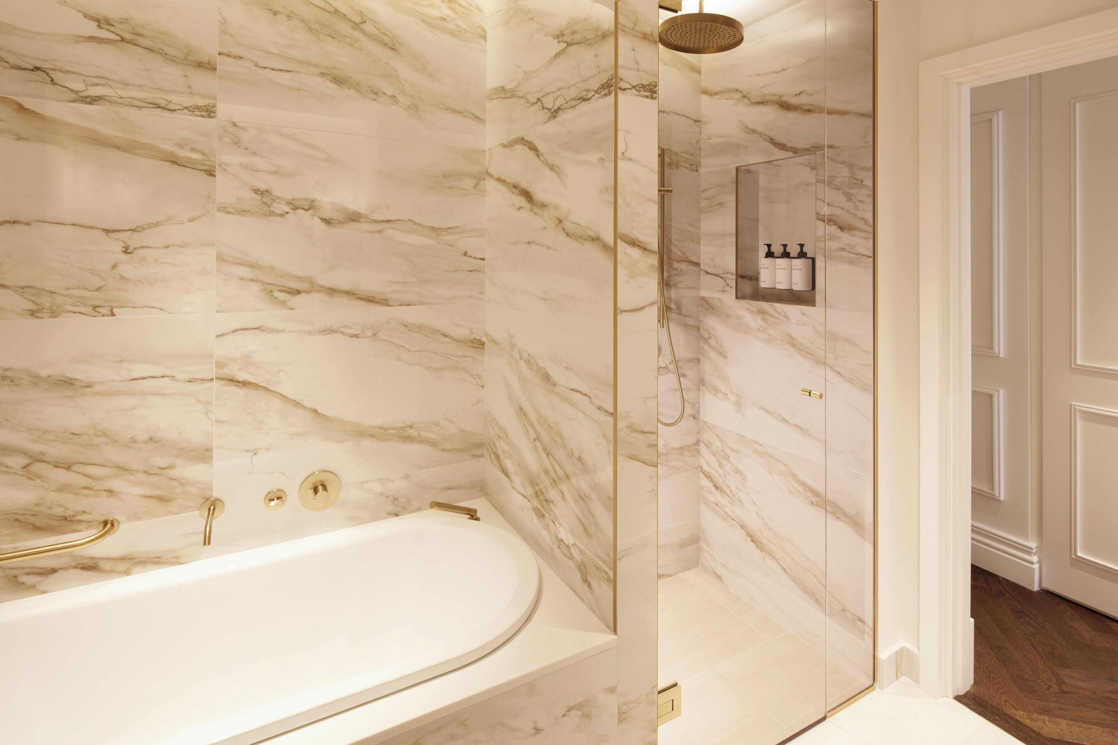 A bathroom with a marble wall, a bathtub, and a shower area.
