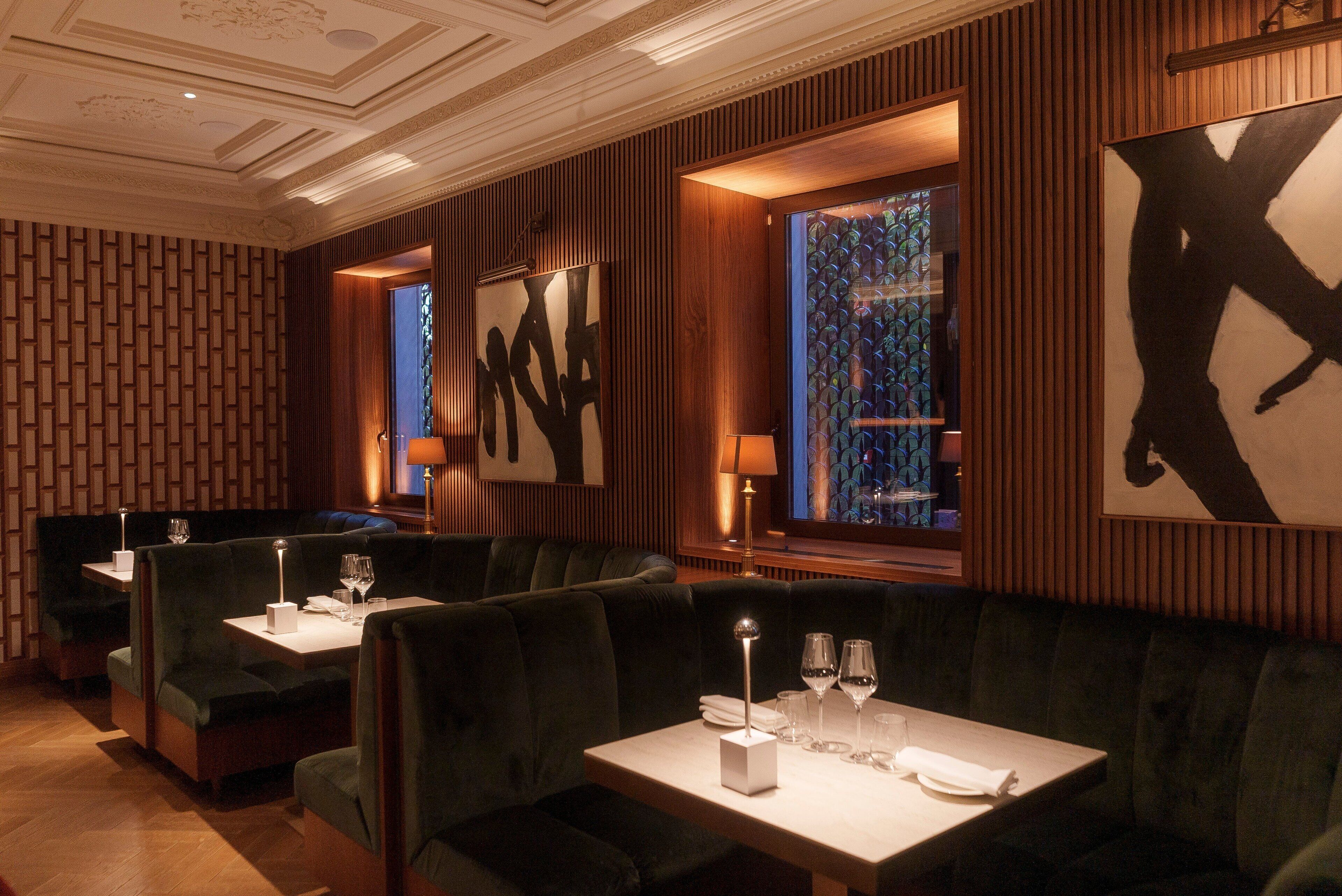 A restaurant with dark green upholstered booths and tables, wooden panel walls, and artwork on the walls.