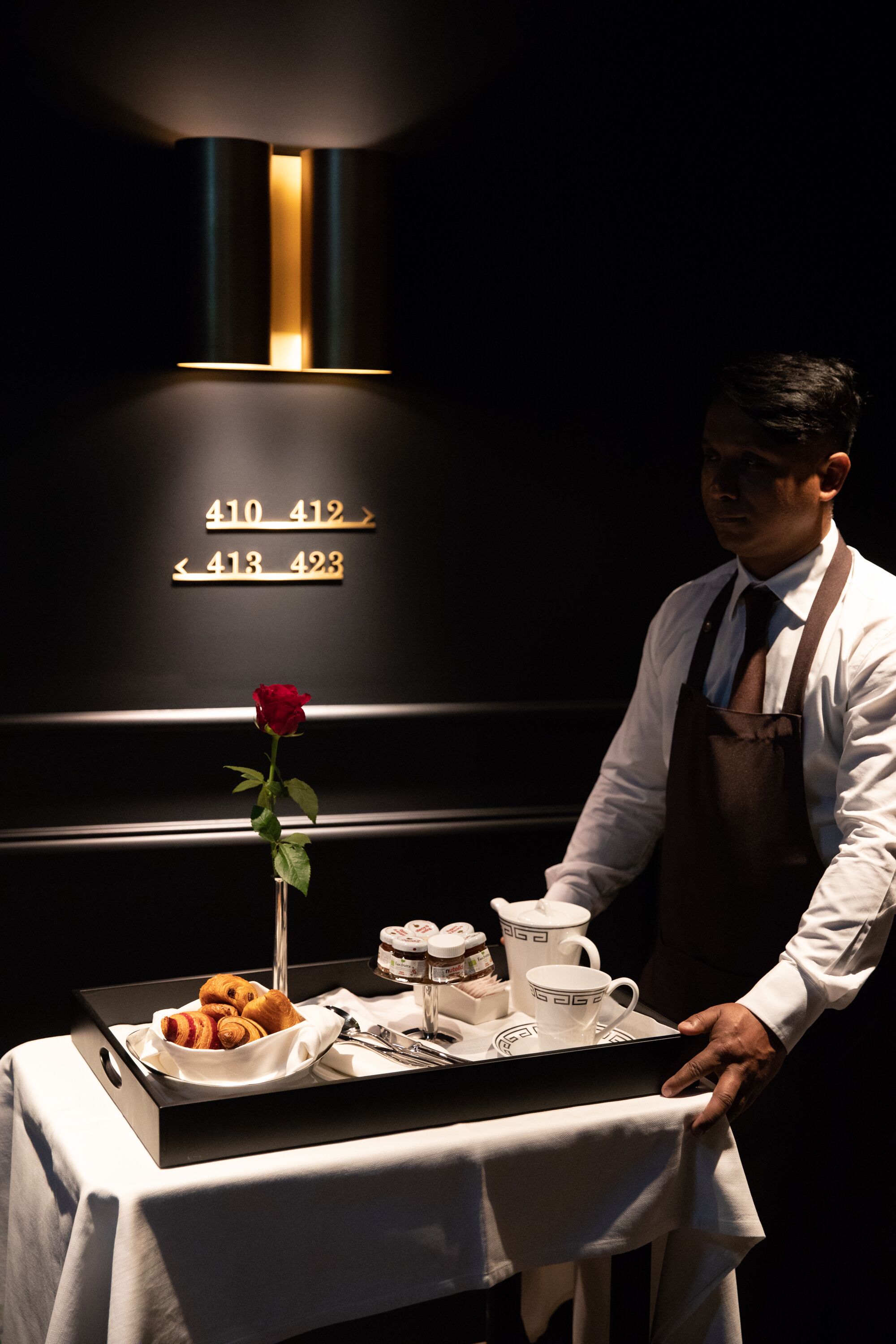 A waiter serving a tray with pastries and a rose to a table.