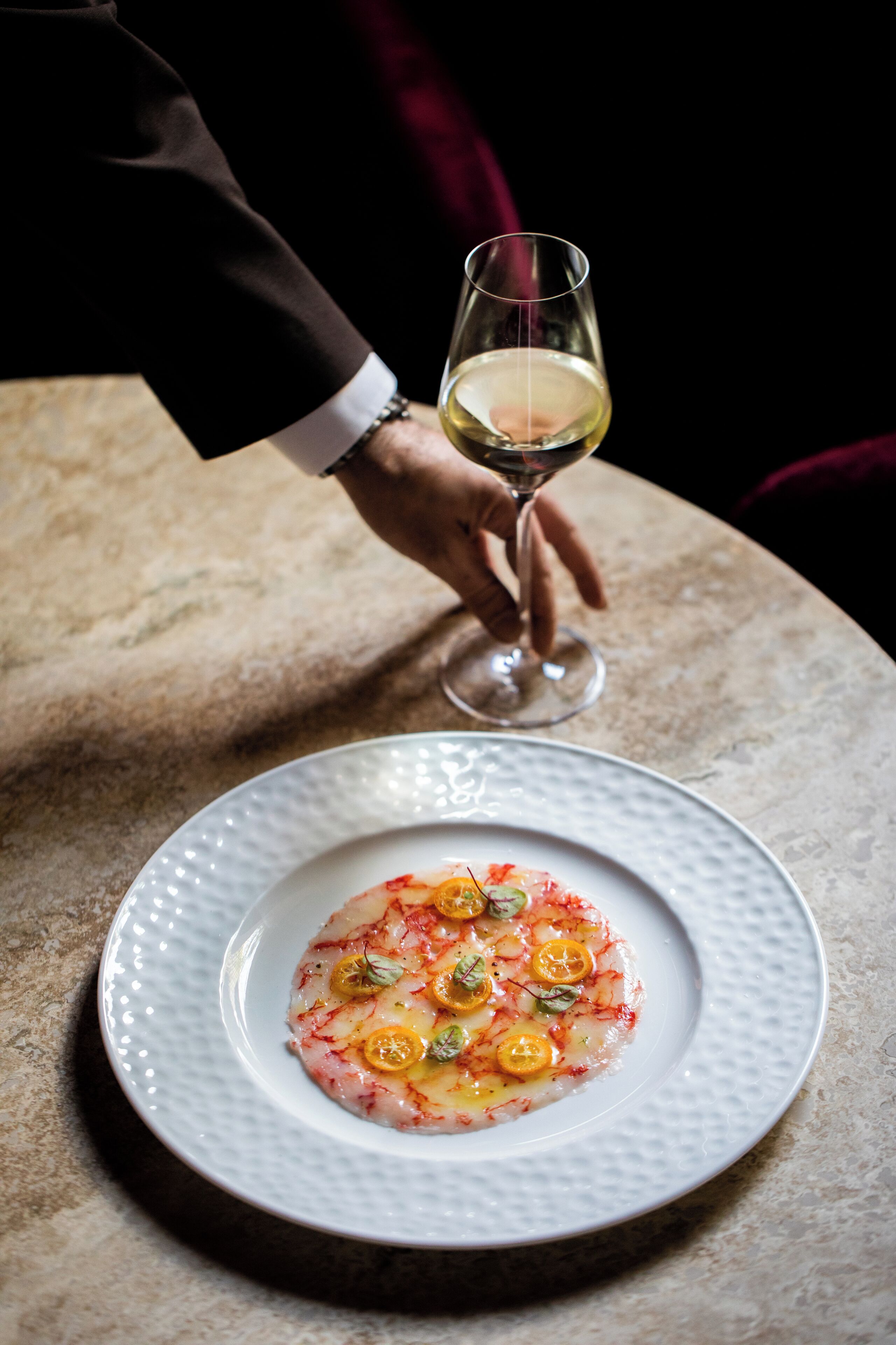 Une assiette blanche contenant un plat de fruits de mer, un verre à vin et une main tenant le verre.