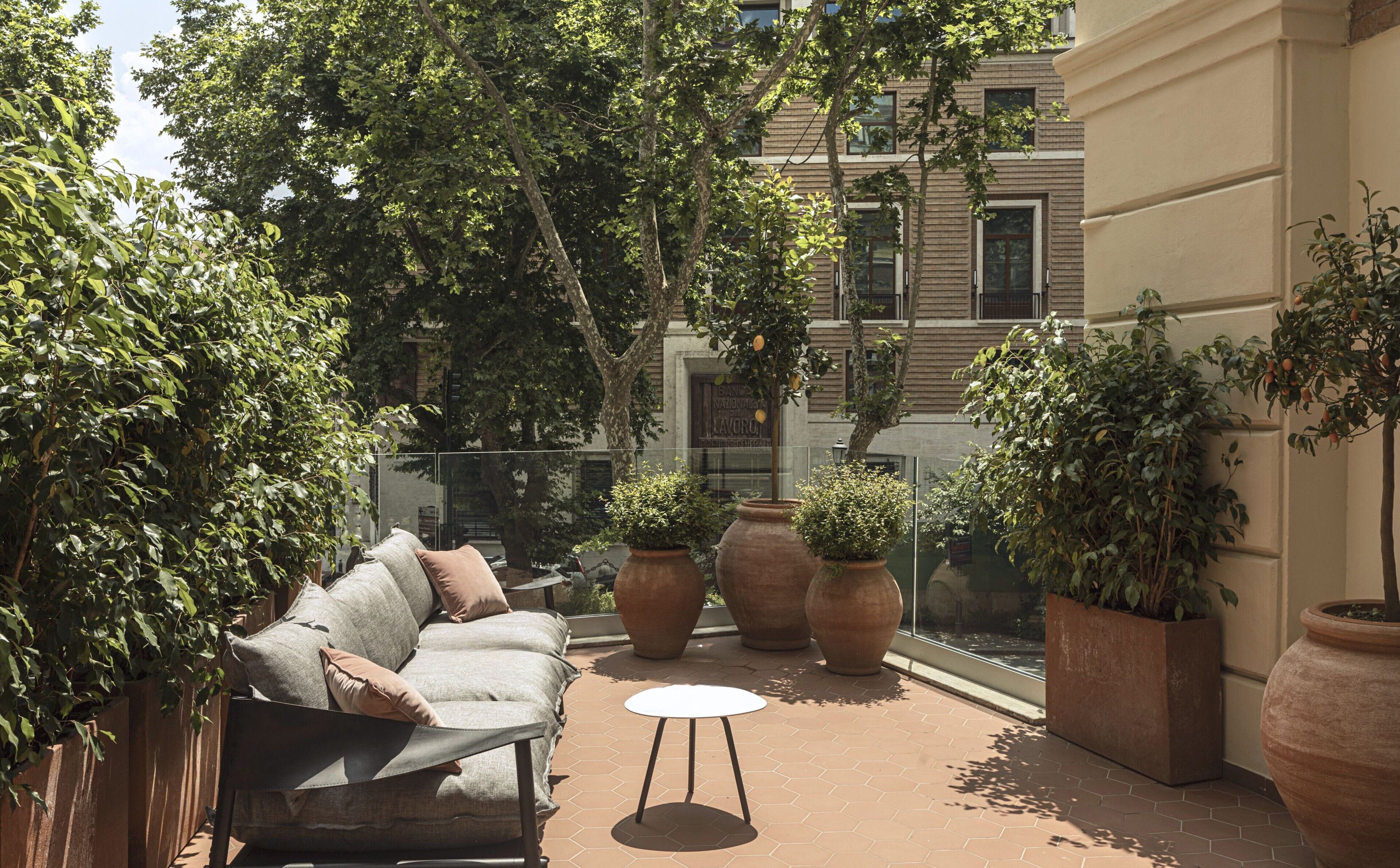 An outdoor seating area with a sofa, a small table, and large potted plants.
