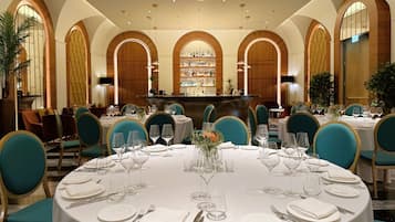A formal dining area with round tables, teal chairs, and a bar in the center.