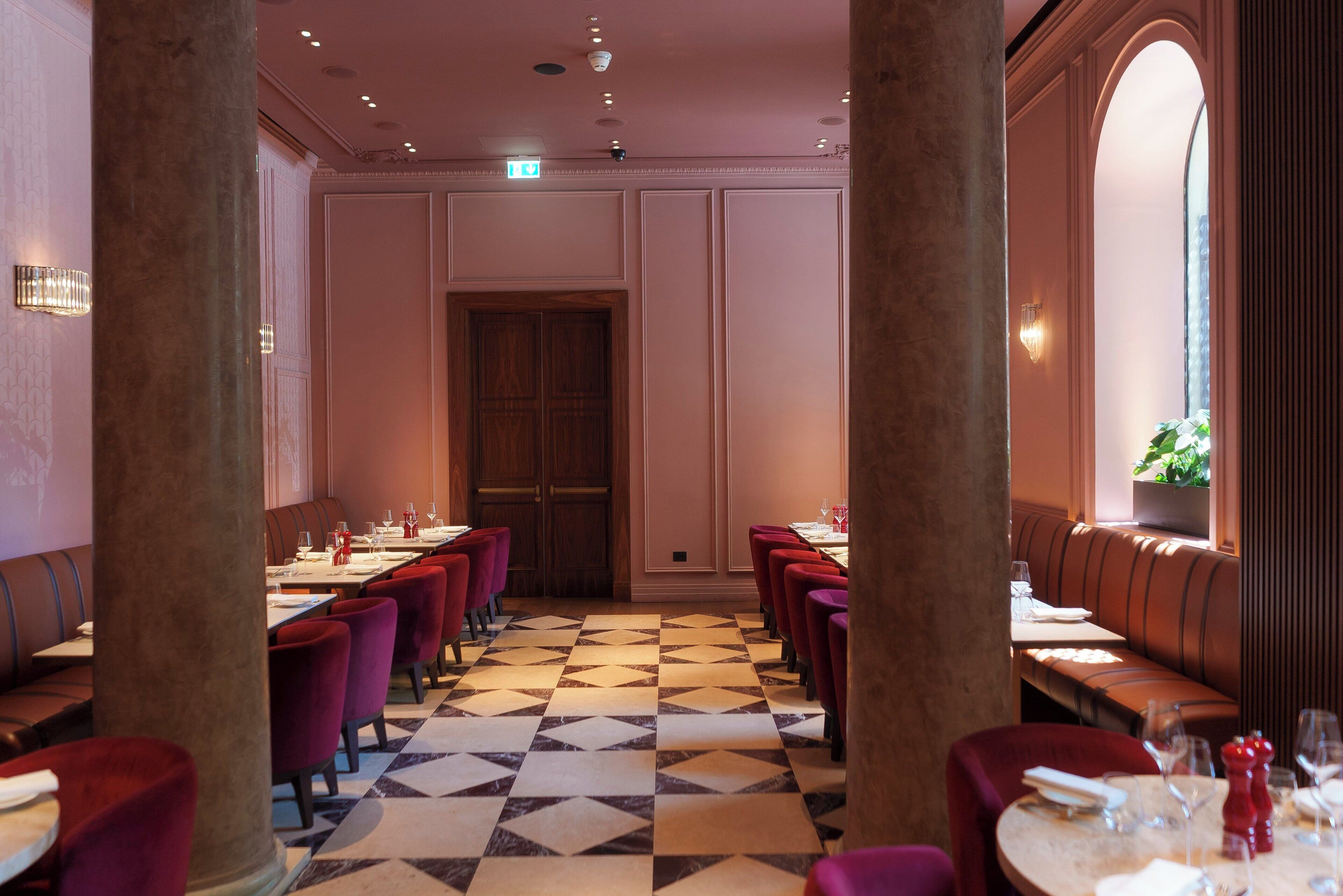 Un restaurante con suelo de tablones, asientos tapizados en rojo y una puerta de madera en el centro.