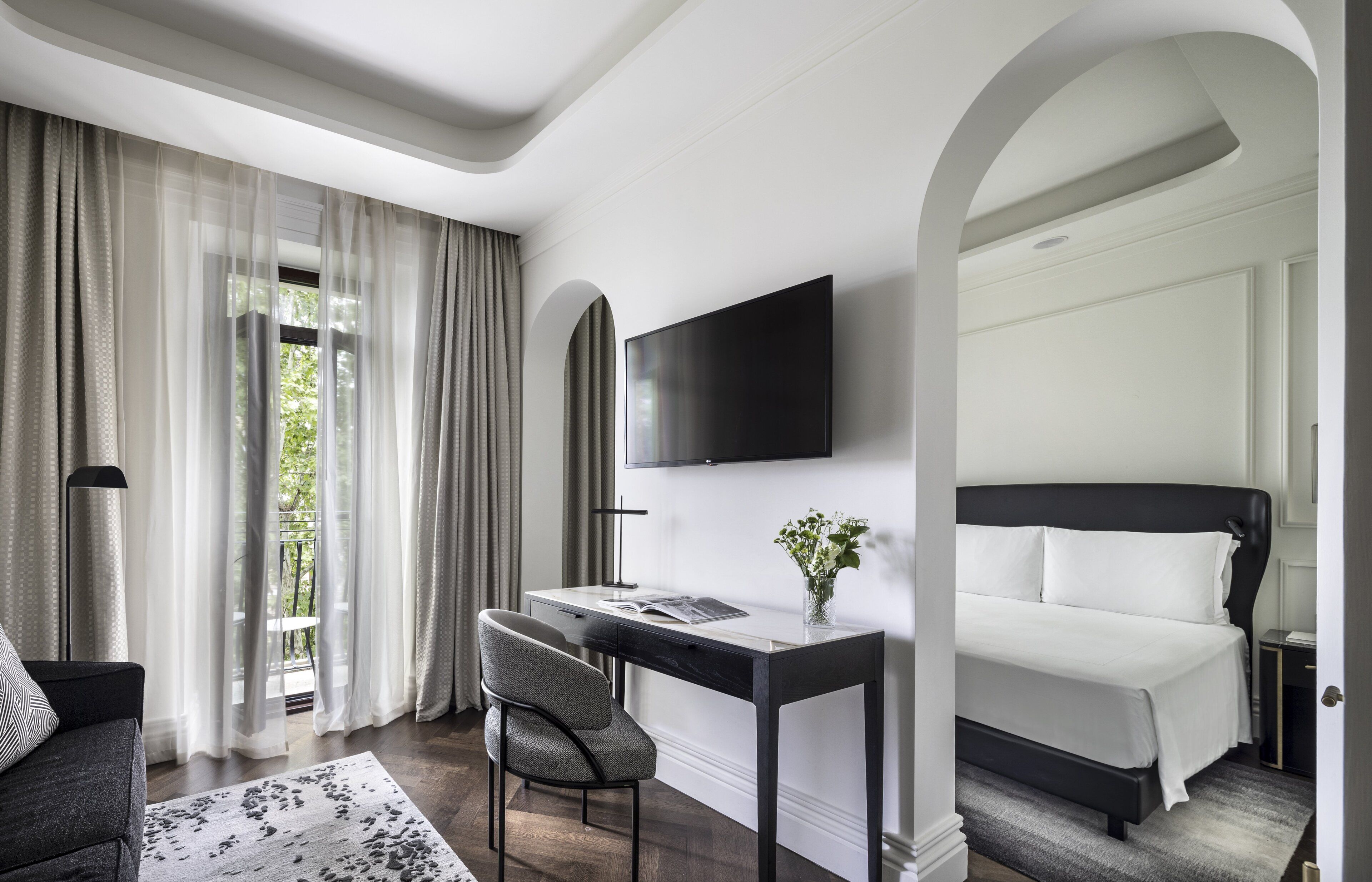 Ein Hotelzimmer mit Bett, Schreibtisch, Stuhl, Flachbildfernseher und Blick auf Grün.