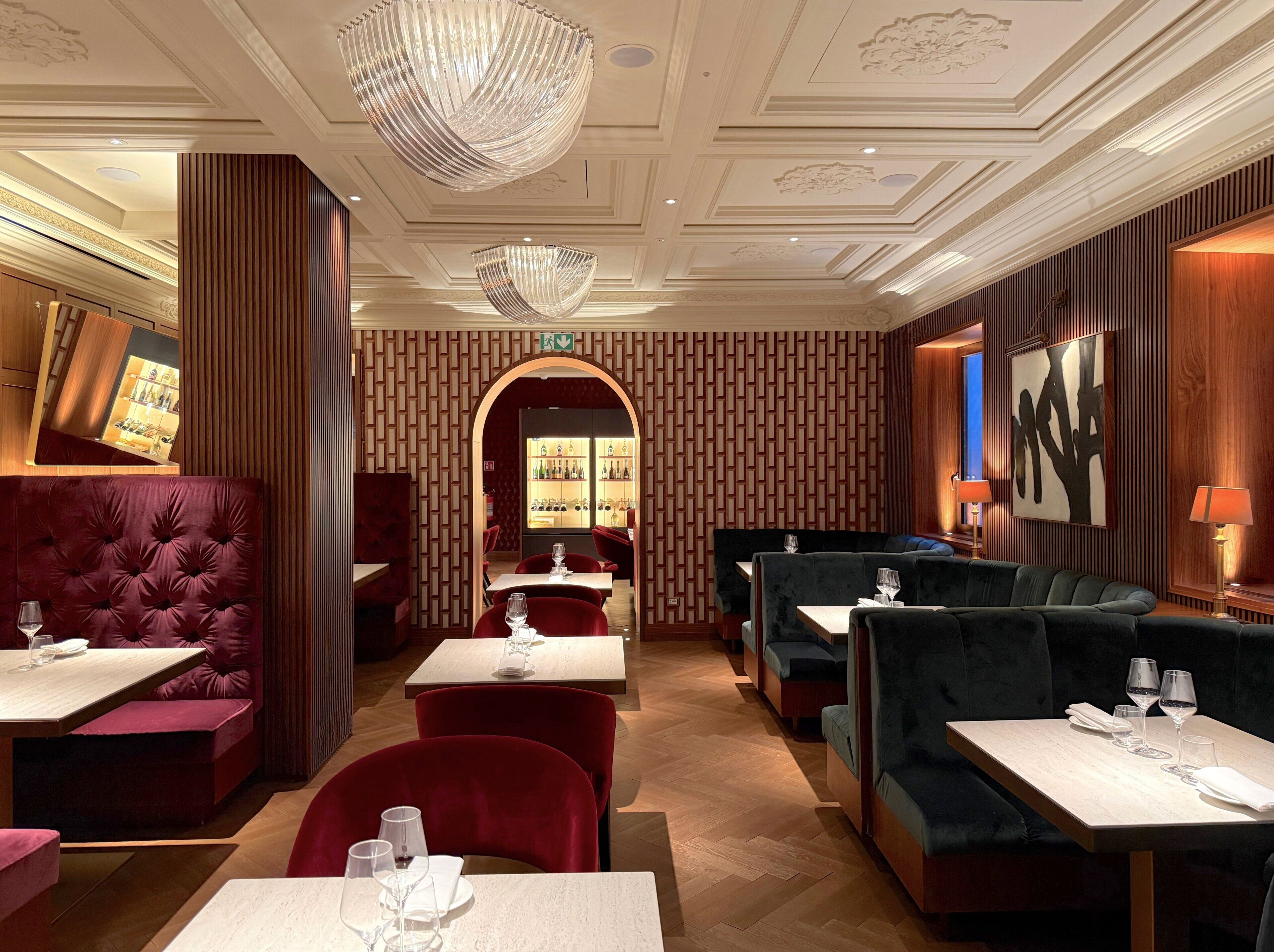 A restaurant interior with plush seating, a bar area, and a chandelier.