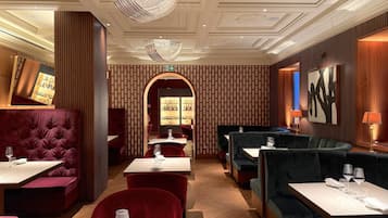 A restaurant interior with plush seating, a bar area, and a chandelier.
