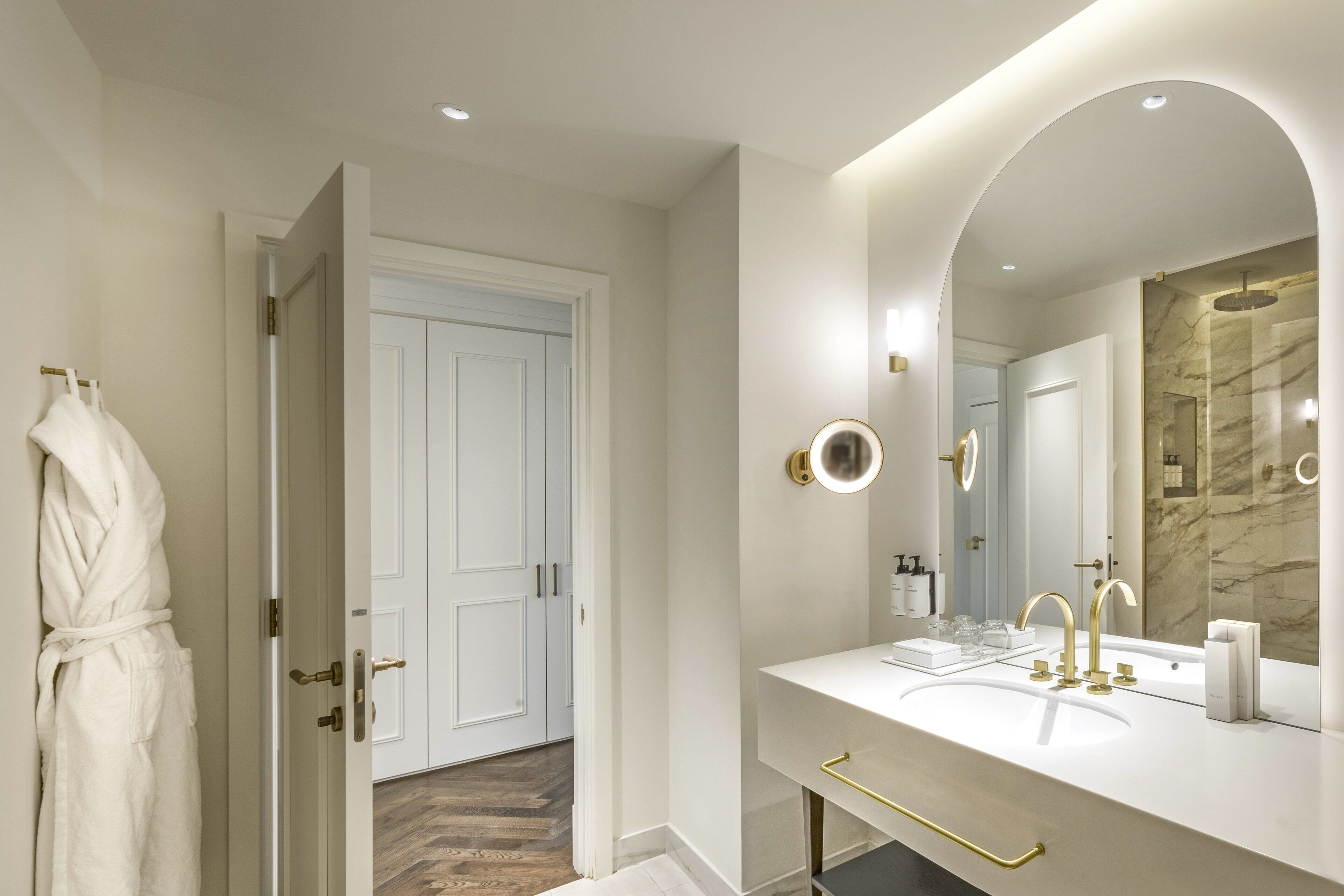 A modern bathroom with a white vanity, gold fixtures, and a marble backsplash.