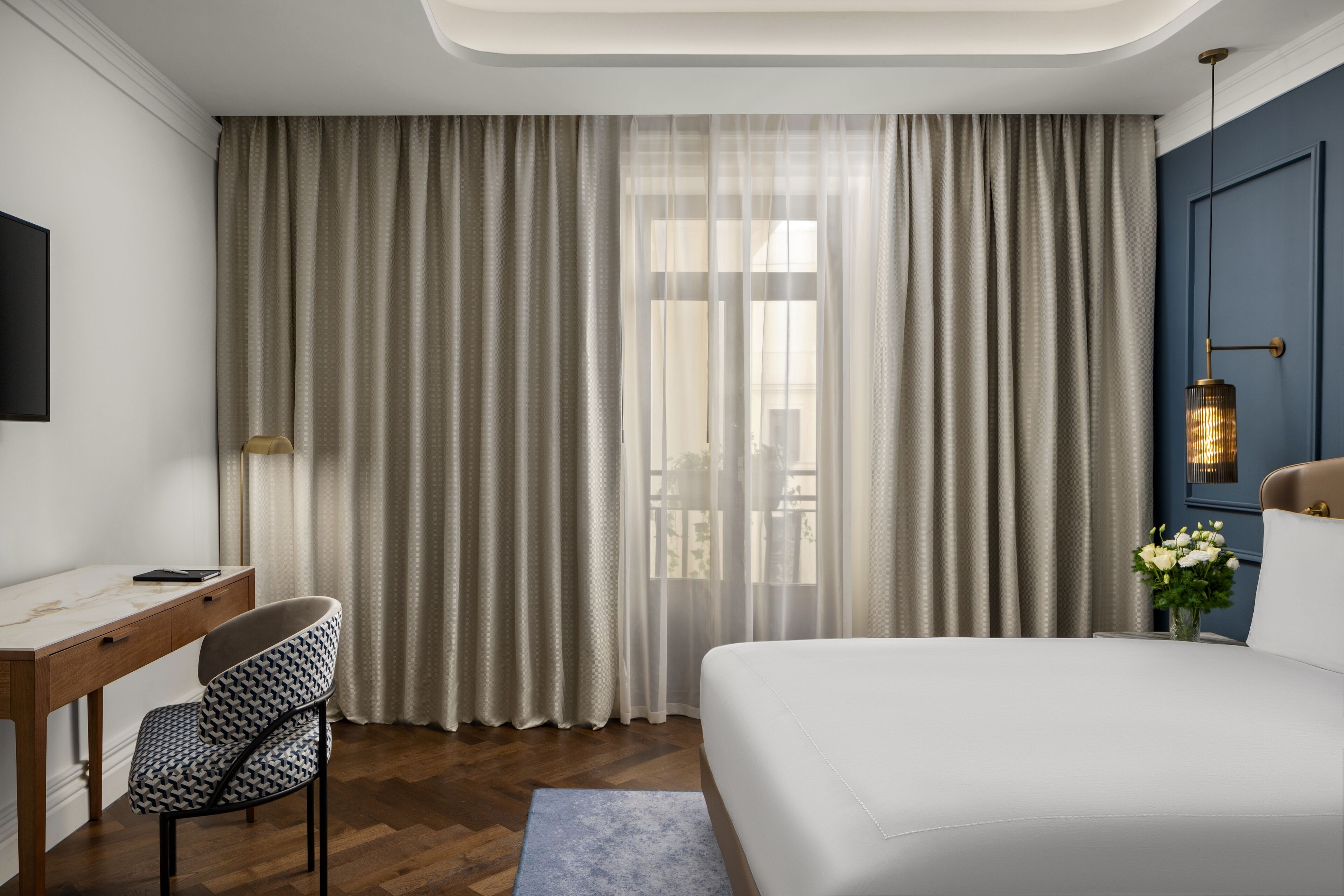 Une chambre d’hôtel moderne équipée d’un lit, d’un bureau, d’une chaise et d’une grande fenêtre avec des rideaux.