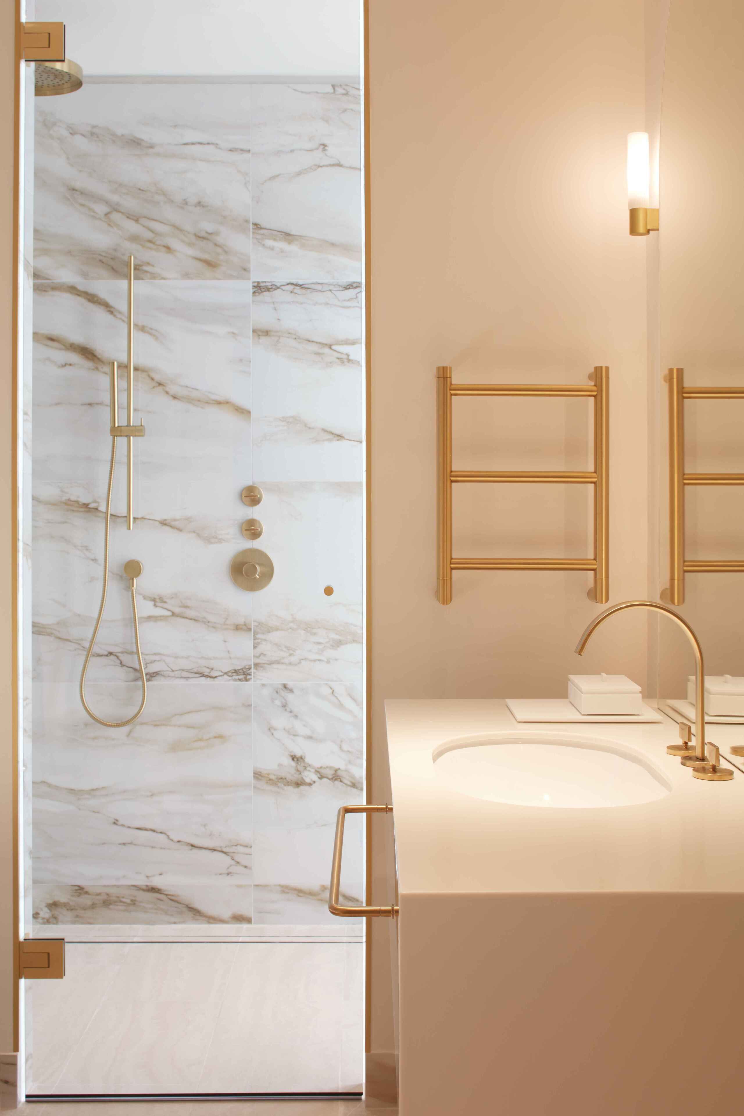A bathroom with a marble wall, a gold showerhead, and a white sink with a gold faucet.
