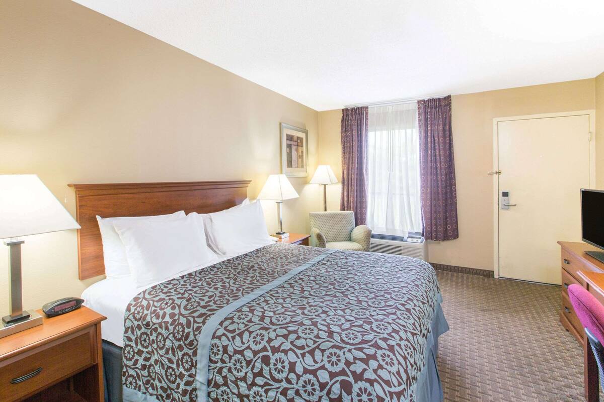 A hotel room with a large bed, two bedside lamps, a chair, a television, and a door.