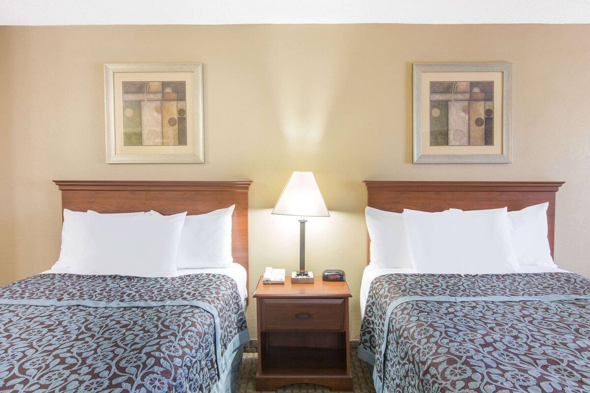 A hotel room with two beds, a nightstand with a lamp, and two framed pictures on the wall.