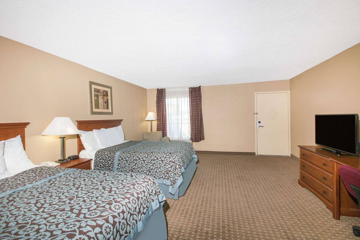 A hotel room with two beds, a TV, a dresser, and a door.