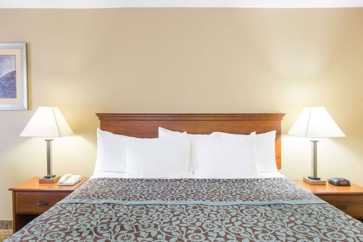 A hotel room with a wooden headboard, two bedside tables with lamps, a telephone, and a patterned bedspread.