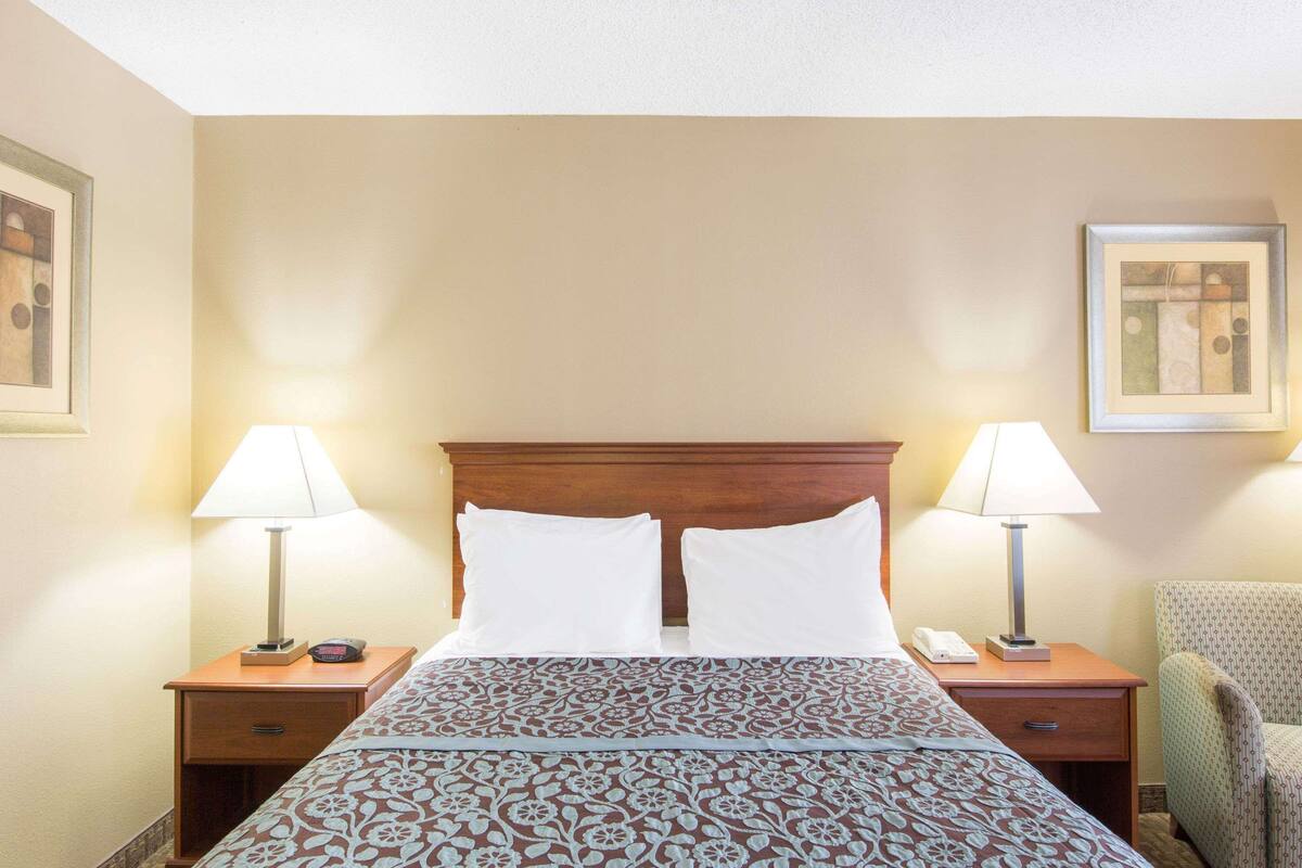 A hotel room with a large bed, two bedside tables with lamps, a chair, and framed artwork on the walls.