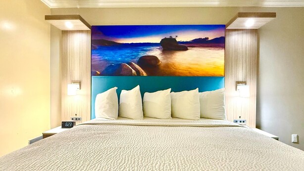 Une chambre d’hôtel avec un grand lit, un tableau représentant un coucher de soleil sur l’eau, accroché au mur, et deux lampes de chevet.