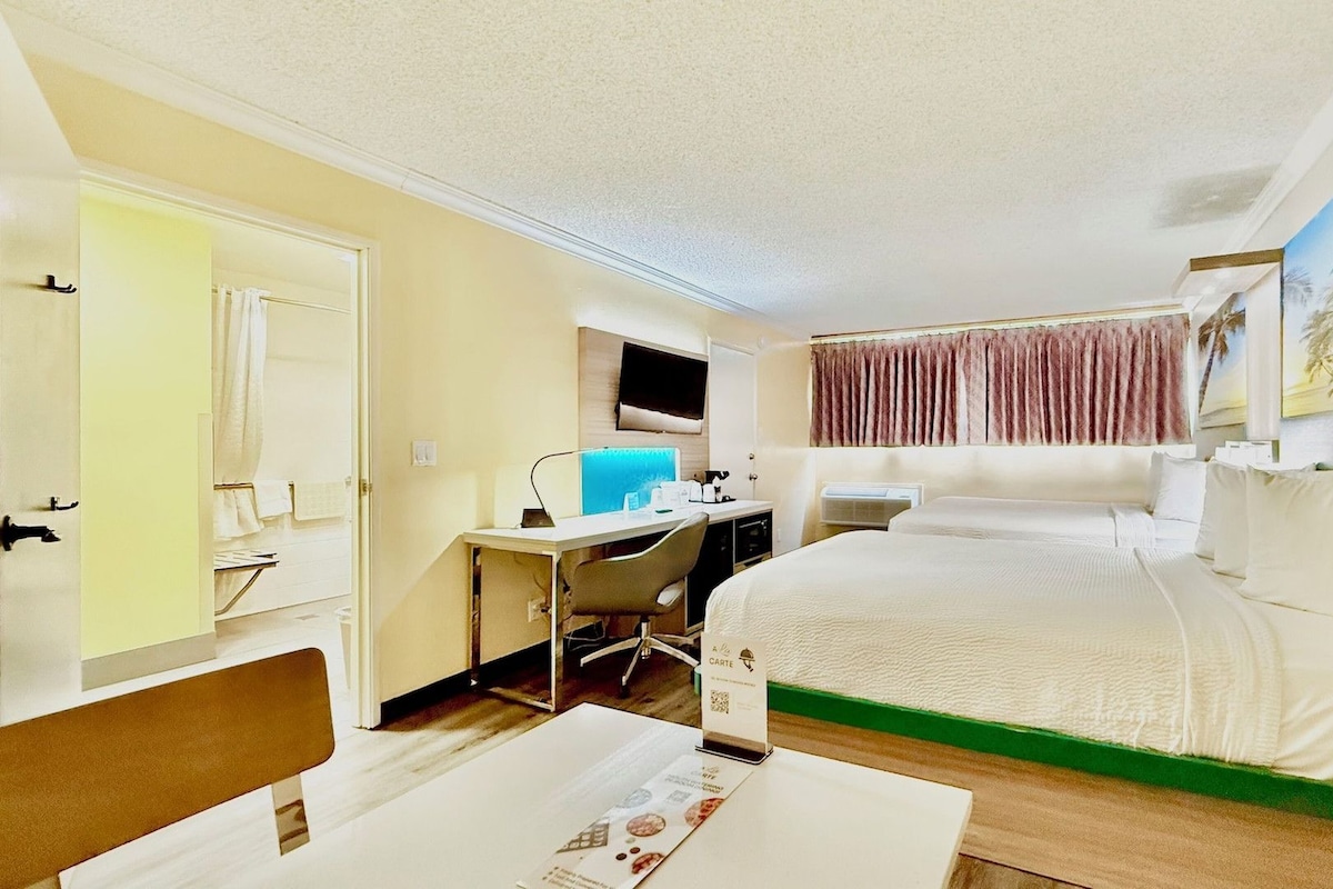Una habitación de hotel con cama, escritorio, silla y un cuadro en la pared.