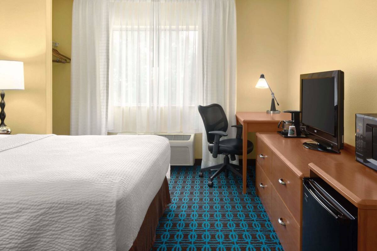 A hotel room with a bed, desk, television, and a microwave.
