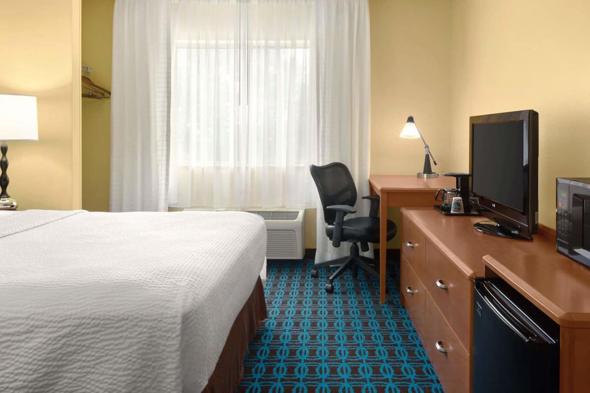 A hotel room with a bed, desk, television, and a microwave.