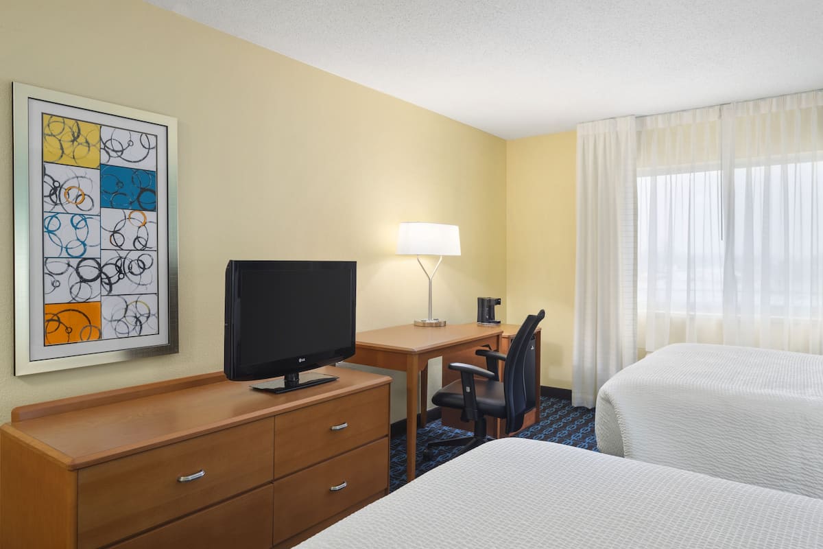 A hotel room with a bed, a desk with a computer, a TV, a lamp, and a framed artwork on the wall.