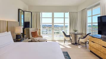 Ein Hotelzimmer mit einem großen Bett, einer Sitzecke mit Stuhl und Tisch, einem Fernseher und einem Balkon mit Stadtblick.
